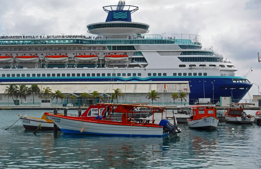 Colorful fishing boats dwarfed by a cruise ship in the harbor